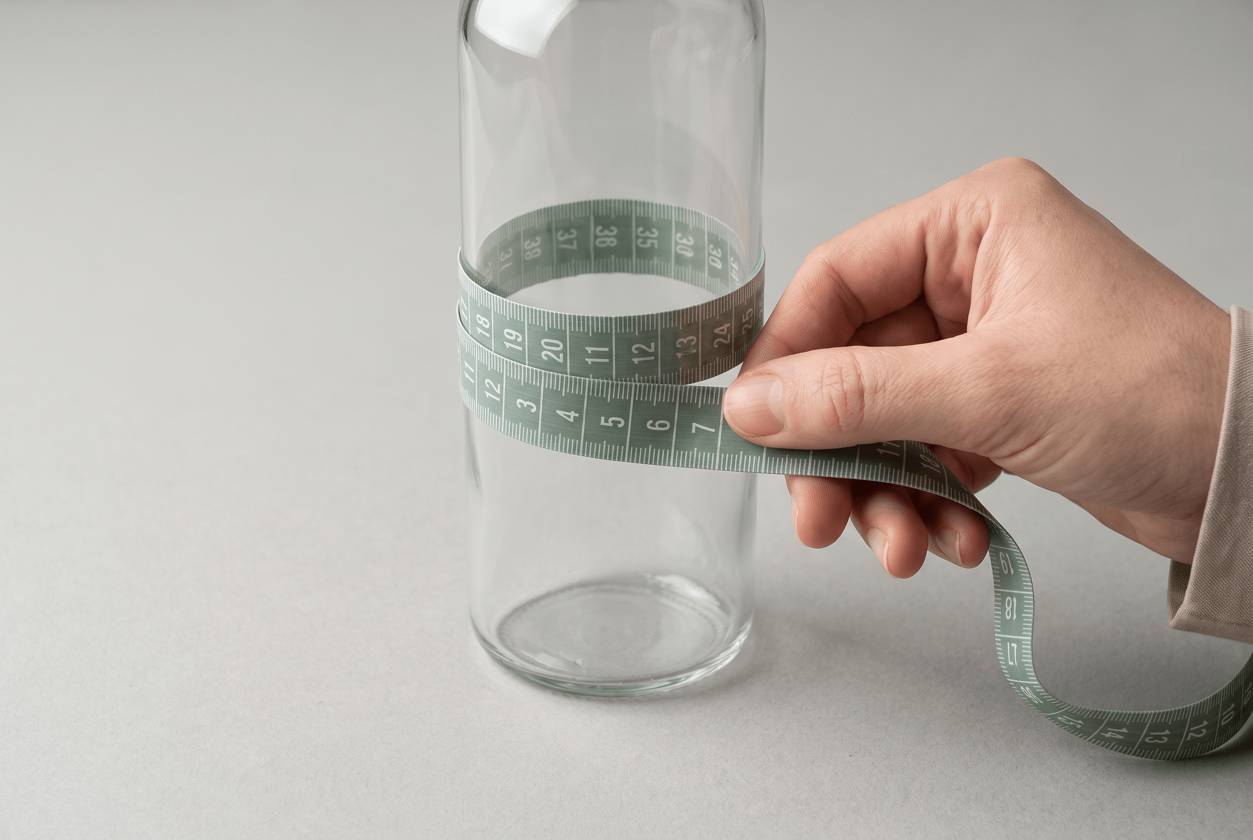 A tape measure wrapped around a bottle to find its circumference for a label